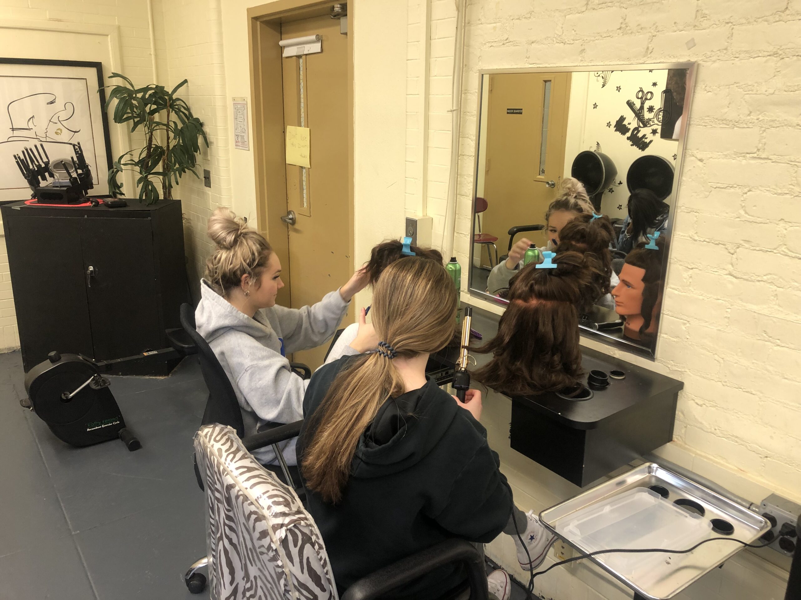 Students in cosmetology are using mannequins to practice their newly learned skills with a curling iron